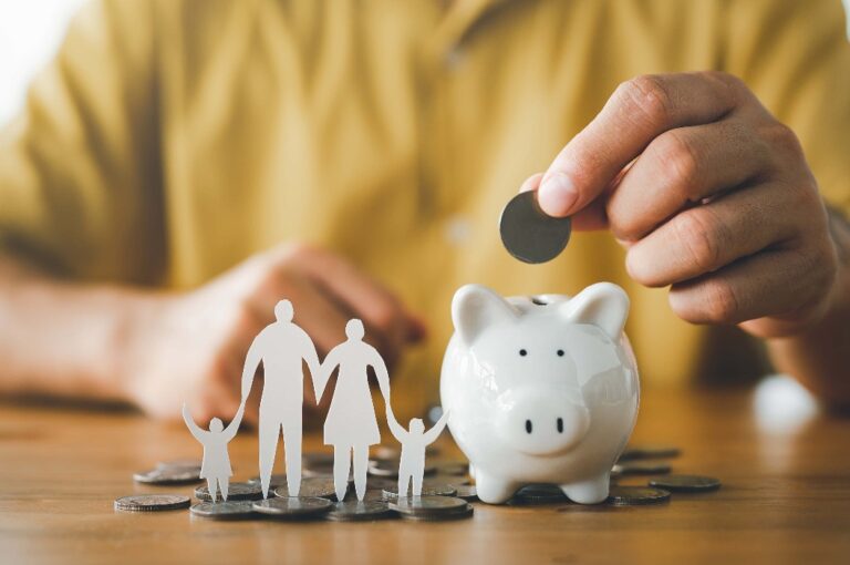 Geschäftsmann legt Münze auf das Sparschwein und Papier Familie auf dem Tisch, Spende, Sparen, Wohltätigkeit, Familie Finanzplan Konzept, Fundraising, Superannuation, Investitionen, Finanzkrise Konzept.